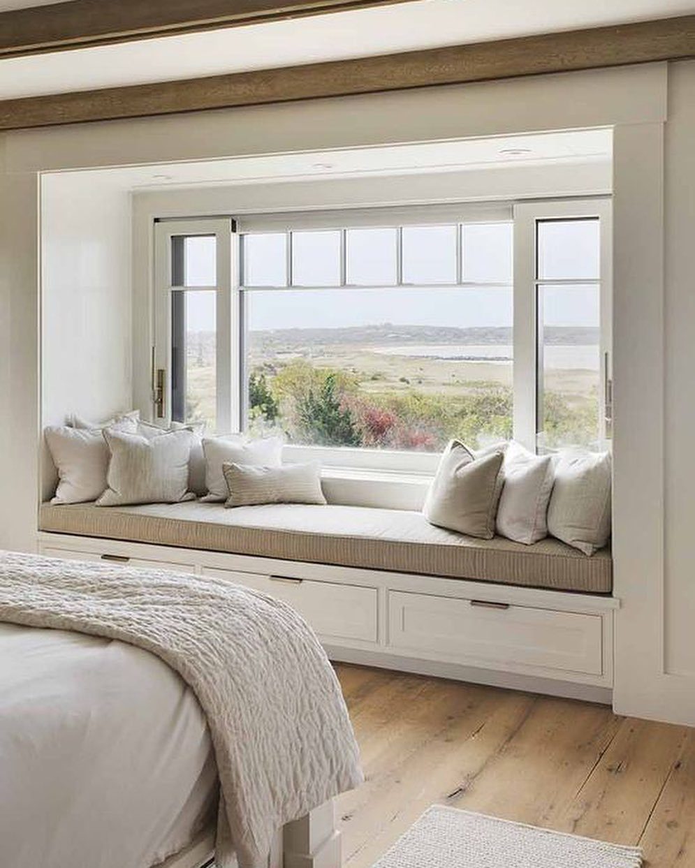 White built-in window seat with beige cushion and storage drawers beneath the seat.