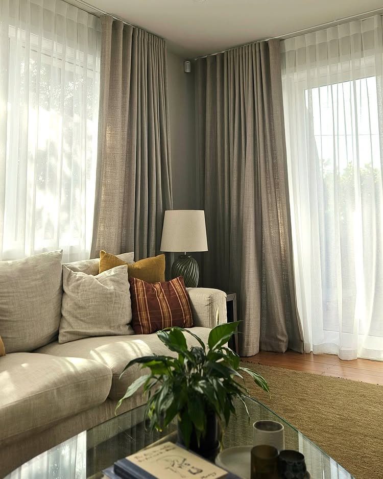 Living room with white sheer curtains paired with taupe drapery panels by a sofa.